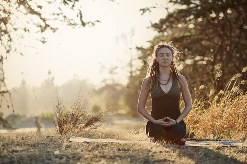 Junge Frau meditiert auf einem Feld - CAVF38147