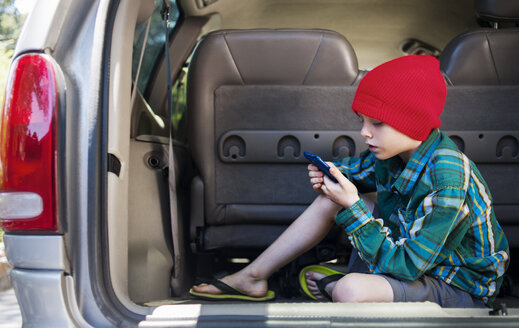 Junge benutzt Mobiltelefon, während er auf dem Rücksitz eines Autos sitzt - CAVF38151