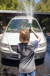 Rückansicht eines Jungen, der sein Auto mit einem Gartenschlauch in der Einfahrt wäscht - CAVF38153