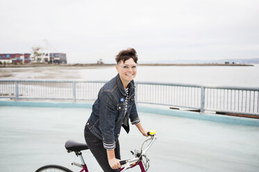 Portrait of happy woman riding bicycle on footpath by sea - CAVF38172