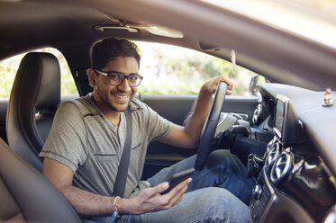 Porträt eines lächelnden Mannes mit Mobiltelefon, der im Auto unterwegs ist - CAVF38196