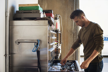 Side view of man taking work tools from cabinet in garage - CAVF38204