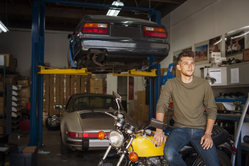 Mann schaut weg, während er in der Garage auf einem Motorrad sitzt - CAVF38205