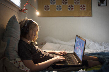 Seitenansicht eines Jungen, der einen Laptop benutzt, während er zu Hause auf dem Bett sitzt - CAVF38212