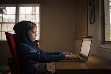 Seitenansicht eines Jungen, der einen Laptop benutzt, während er zu Hause sitzt - CAVF38215