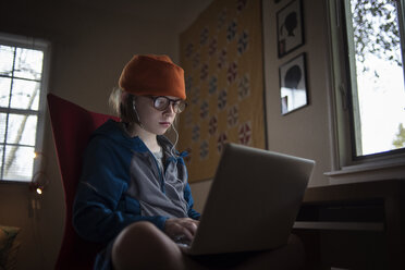 Junge, der einen Laptop benutzt, während er auf einem Stuhl am Tisch zu Hause sitzt - CAVF38217