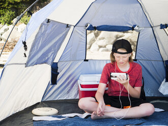 Junge benutzt Smartphone, während er im Zelt sitzt - CAVF38234