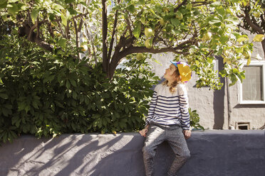 Junge sitzt auf einer Stützmauer und betrachtet die Früchte, die an einem Baum wachsen - CAVF38235