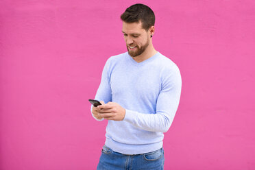Young man texting with smartphone, pink background - JSMF00141