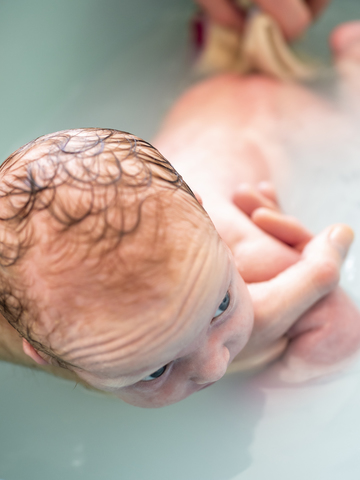 Mann badet neugeborenes Mädchen in einer Wanne, lizenzfreies Stockfoto