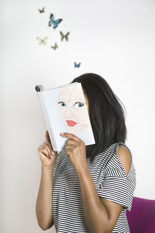 Frau bedeckt Gesicht mit Buch, liest Gedichte mit Schmetterlingen, lizenzfreies Stockfoto