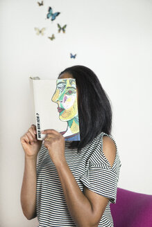 Woman covering face with book, reading poetry with butterflies - PSTF00101