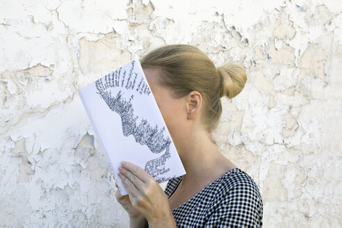 Frau bedeckt ihr Gesicht mit einem Buch und liest Gedichte vor einer Wand - PSTF00103