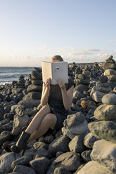 Woman covering face with book, reading poetry, eye looking through cover - PSTF00109