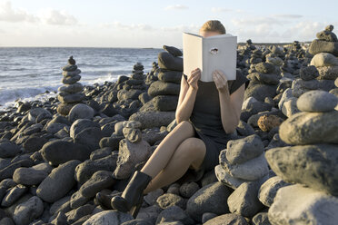 Woman covering face with book, reading poetry, eye looking through cover - PSTF00110