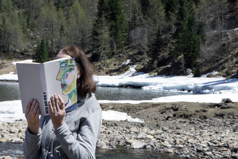 Frau bedeckt ihr Gesicht mit einem Buch und liest Gedichte in den Bergen - PSTF00111