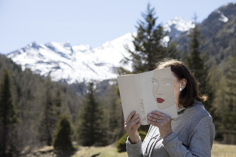 Woman covering face with book, reading poetry in the mountains stock photo