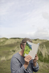 Mann bedeckt sein Gesicht mit einem Buch und liest Gedichte in den Dünen - PSTF00116