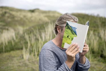 Mann liest in den Dünen ein Märchenbuch und verdeckt sein Gesicht - PSTF00117