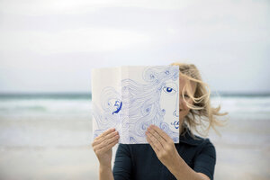 Frau bedeckt ihr Gesicht mit einem Buch und liest Gedichte am Strand - PSTF00120