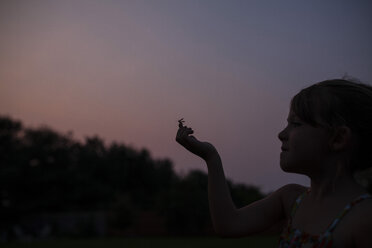 Mädchen mit Insekt am Finger vor klarem Himmel bei Sonnenuntergang - CAVF38298