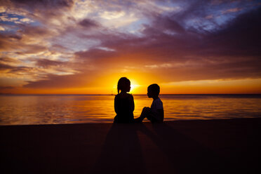 Silhouette Geschwister sitzen am Strand bei Sonnenuntergang - CAVF38314