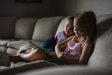 Siblings looking at picture book on sofa - CAVF38319