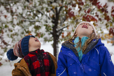 Playful siblings sticking out tongue while standing outdoors during winter - CAVF38324