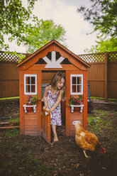 Happy girl looking at hen while standing on entrance of chicken coop - CAVF38327