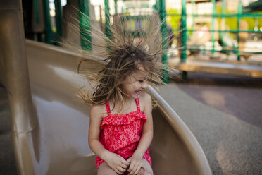 Happy girl playing flicking hair while sitting on slide - CAVF38331