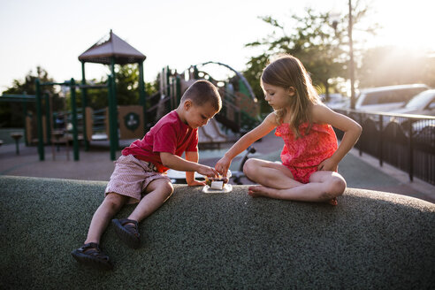 Geschwister beim Essen auf dem Spielplatz bei Sonnenuntergang - CAVF38332