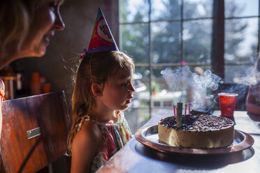 Girl looking at birthday cake with mother at home - CAVF38335