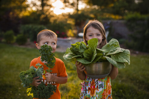 Glückliche Geschwister, die im Hinterhof stehend Gemüse tragen - CAVF38344
