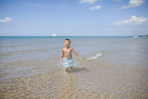Fröhlicher Junge läuft im Meer gegen den Himmel an einem sonnigen Tag - CAVF38361