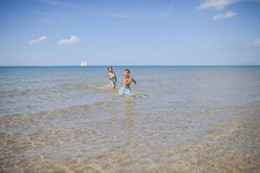 Playful siblings running in sea against sky on sunny day - CAVF38362