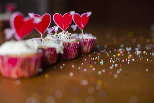 Mit herzförmigen Stäbchen verzierte Cupcakes auf dem Holztisch - CAVF38368