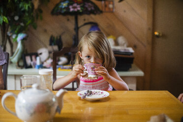 Porträt eines Mädchens, das am Holztisch sitzend Kaffee trinkt - CAVF38380