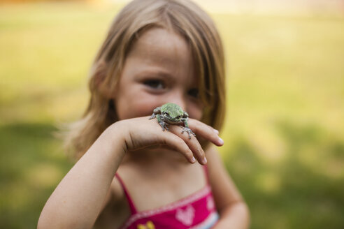 Porträt eines verspielten Mädchens mit Frosch im Hof stehend - CAVF38383