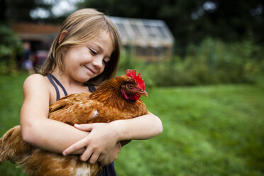 Smiling girl holding hen while standing in yard - CAVF38393