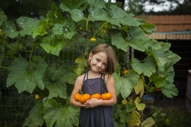 Portrait of smiling girl holding pumpkins while standing against plants - CAVF38401