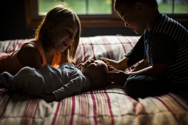 Siblings playing with baby girl on bed at home - CAVF38412