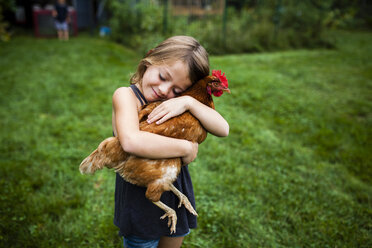 Smiling girl with eyes closed holding hen while standing in yard - CAVF38415