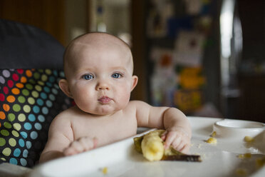 Porträt des niedlichen hemdlosen Baby-Mädchens mit Banane auf dem Hochstuhl sitzend - CAVF38442