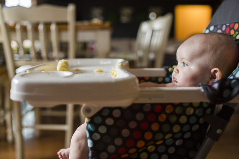 Baby girl looking away while sitting on high chair at home stock photo