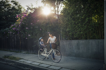 Woman looking at son sitting on bicycle back seat outdoors - MASF03760