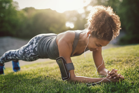 Woman doing plank exercise on grassy field at park stock photo