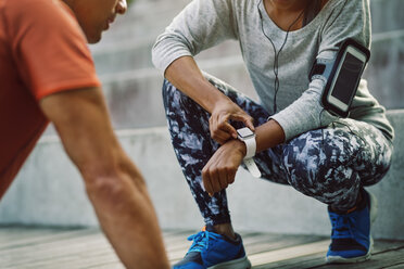 Woman using smart watch while friend doing push-ups on steps - MASF03782