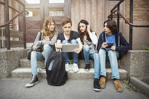 Jugendliche benutzen ein Tablet, während sie auf einer Treppe im Freien sitzen - MASF03789