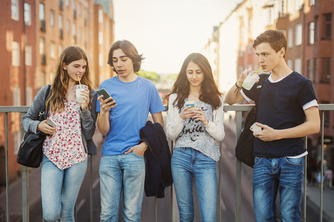 Teenagers using smart phone while drinking juice on bridge in city stock photo