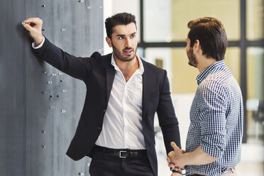 Young businessman pinning paper on notice board while talking with colleague in office - MASF03800